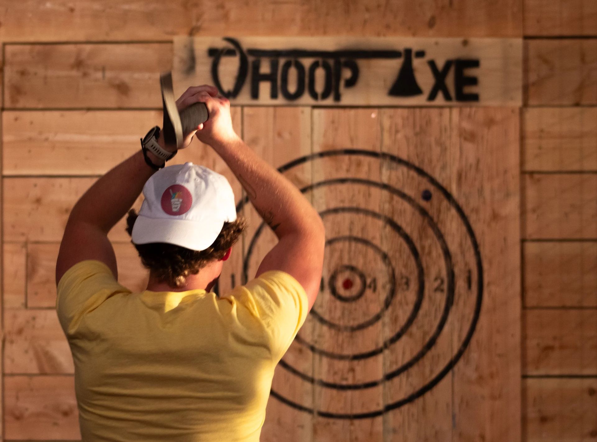 Guest mid-throw, axe raised behind her head, aiming at a Whoop Axe bullseye target
