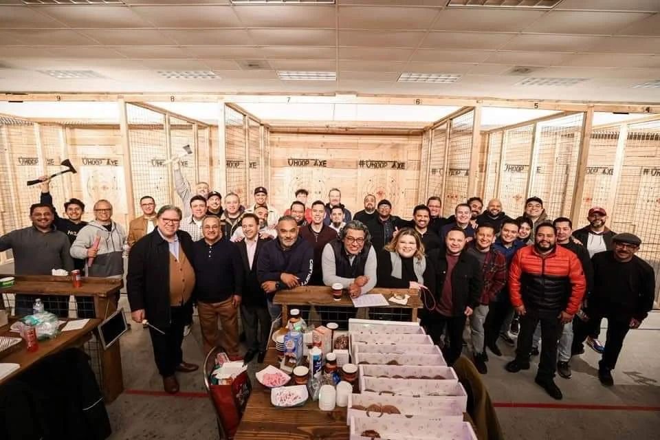 A company group of about 40 people posing together in front of the Whoop Axe throwing lanes
