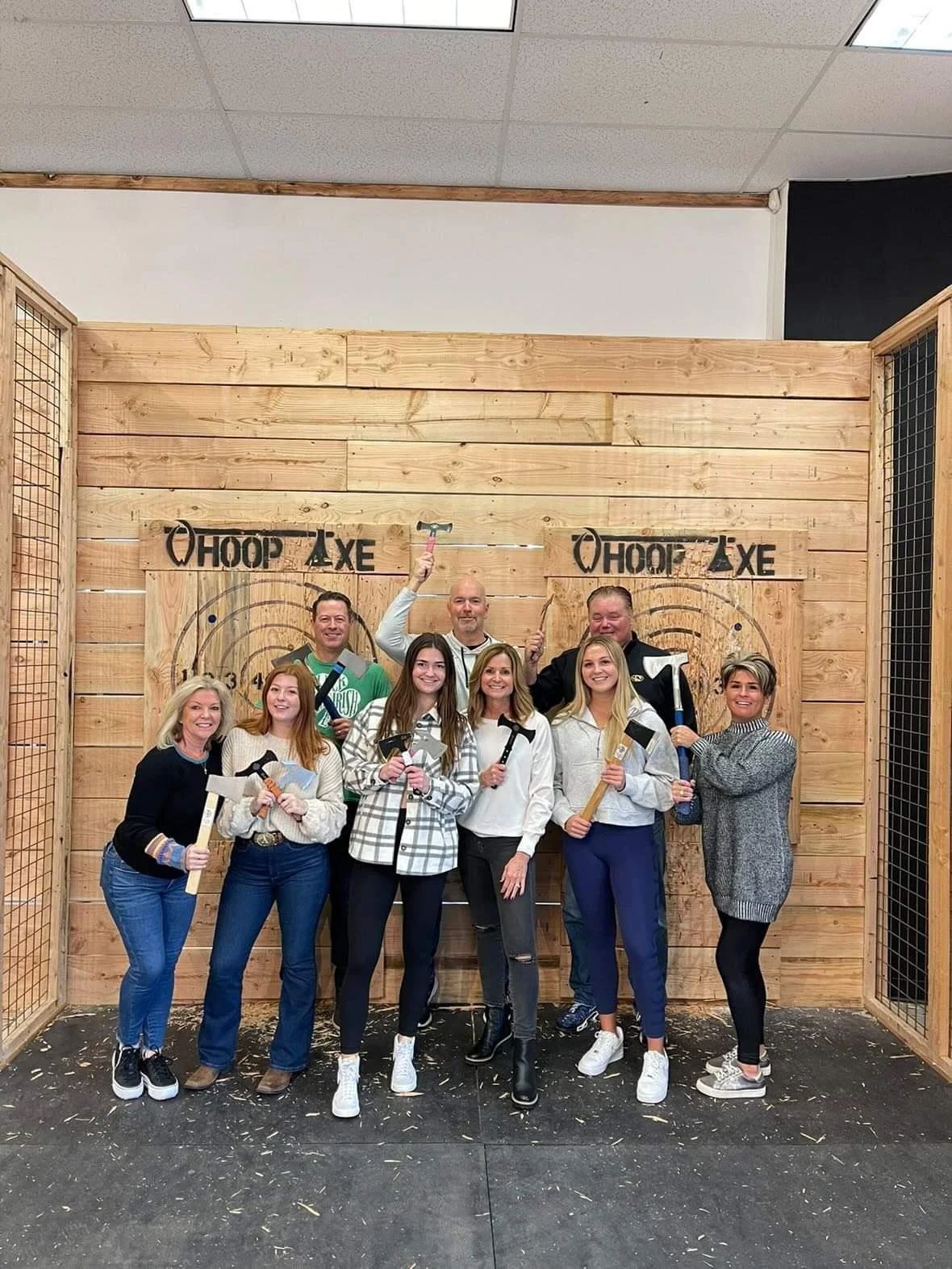 Eight guests holding axes in front of the branded wooden targets in a Whoop Axe lane