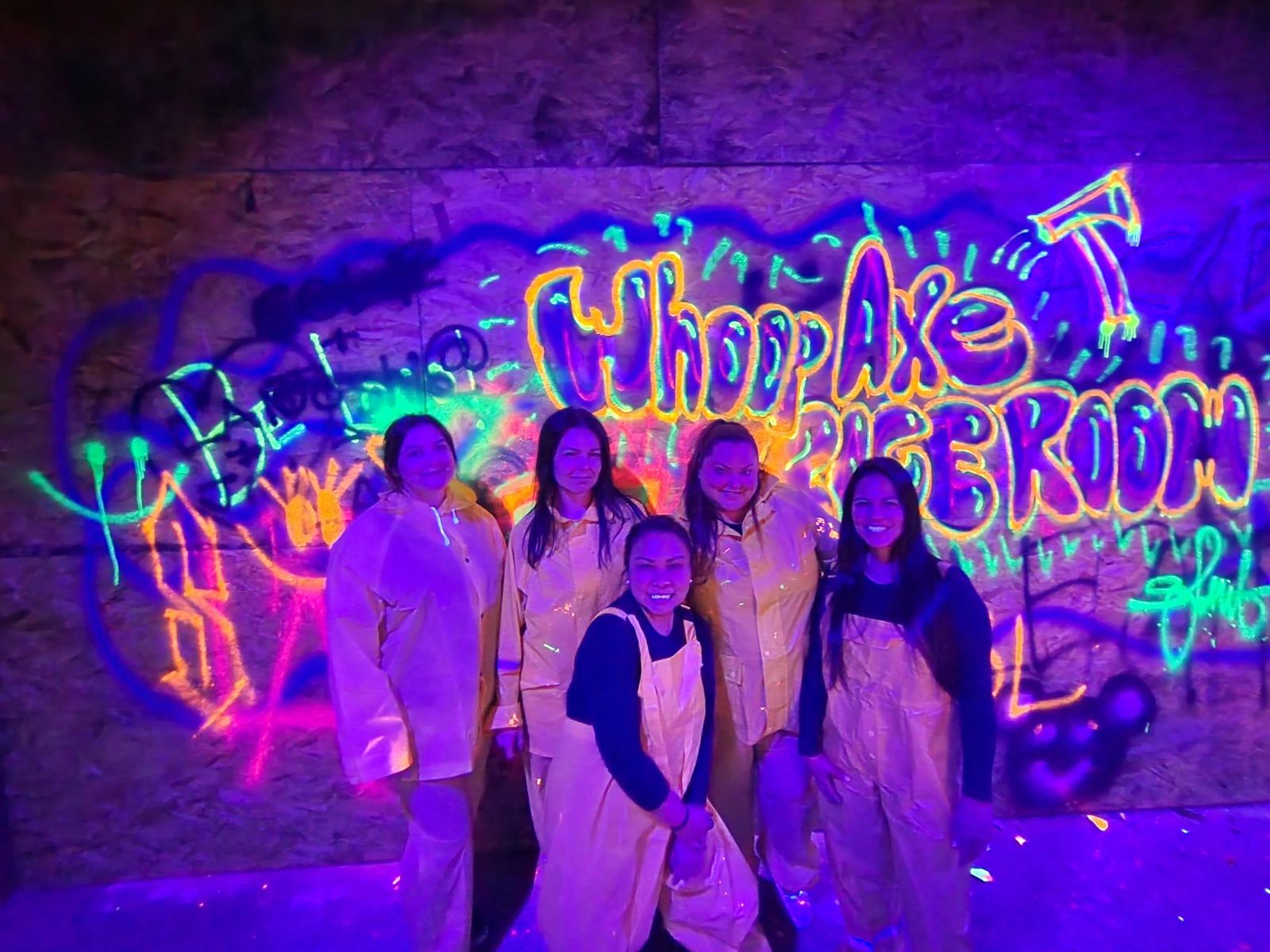 Group in protective suits in front of the glowing Whoop Axe Rage Room graffiti wall